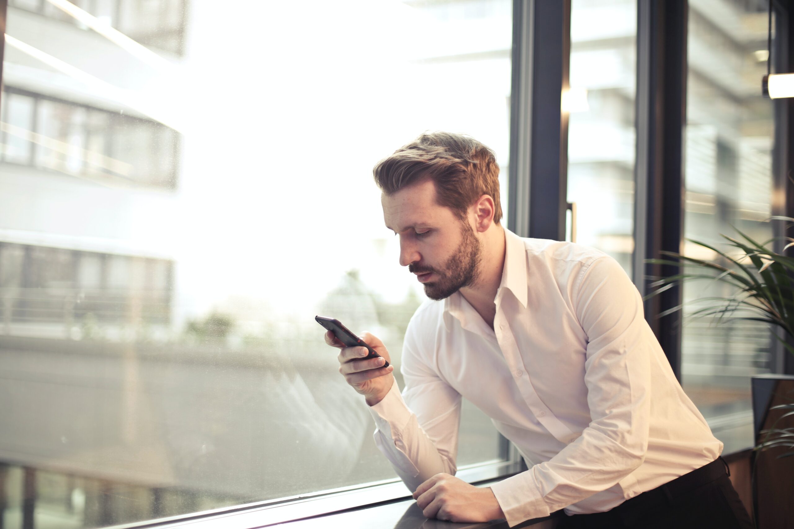 photo-of-man-in-white-dress-shirt-holding-phone-near-window-859265